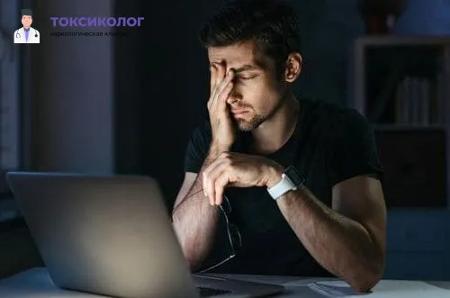 Уставший мужчина за компьютером, испытывающий симптомы, требующие лечения сонливости